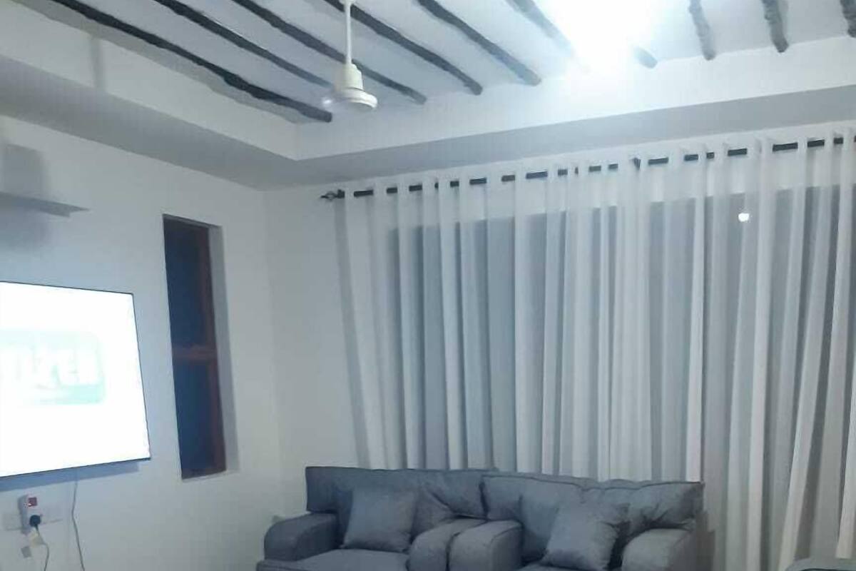 A modern living room with a grey sofa, a black armchair, and a TV mounted on the wall.