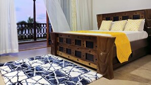 Un dormitori amb un llit, un panell de fusta al capçal, una manta groga i una catifa amb dibuixos.