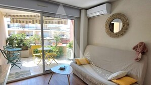 A living room with a sofa, a small table, and a chair. There is a sliding glass door leading to an outdoor area with a table and chairs. - T2 moderne avec belle terrasse (Sète)