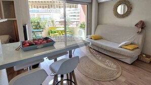 A modern living room with a glass dining table, a sofa with cushions, a round rug, and a view of the outside balcony. - T2 moderne avec belle terrasse (Sète)