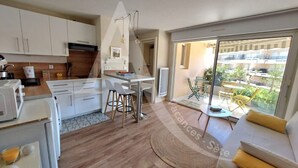 A modern kitchen with white cabinets, a dining area with a table and chairs, and a living area with a sofa and a view of a balcony. - T2 moderne avec belle terrasse (Sète)