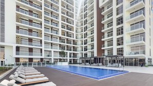 A modern apartment building with a rooftop pool area, lounge chairs, and outdoor seating. - WelHome - Cozy Studio Apt. with Private Balcony in Arjan (Dubai)
