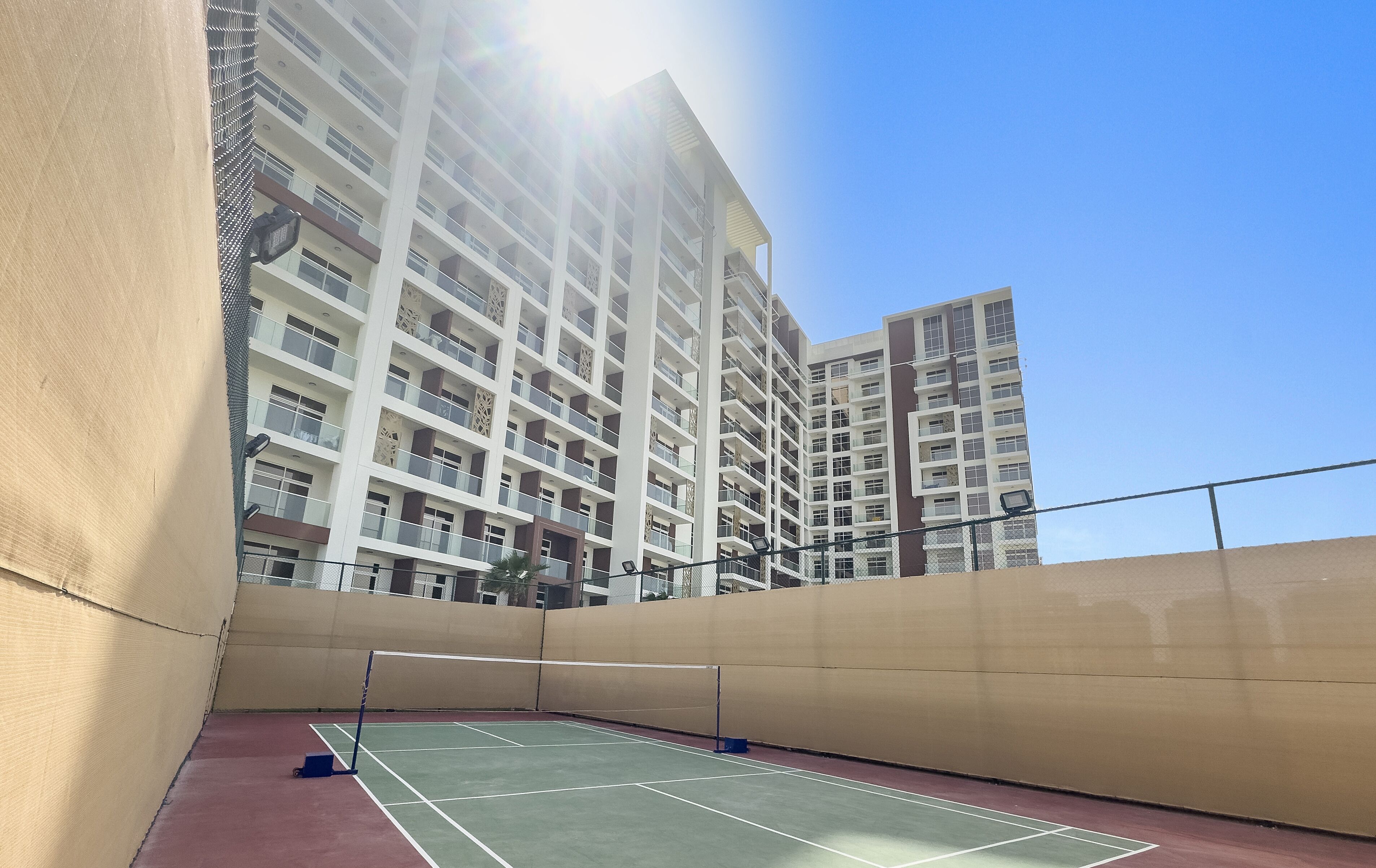 An indoor tennis court with a net, surrounded by beige walls and a high-rise building in the background.