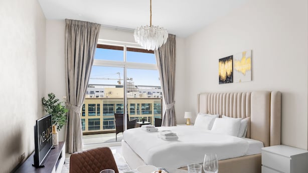 A modern hotel room with a large bed, a television, a desk, and a view of the cityscape. - WelHome - Cozy Studio Apt. with Private Balcony in Arjan (Dubai)