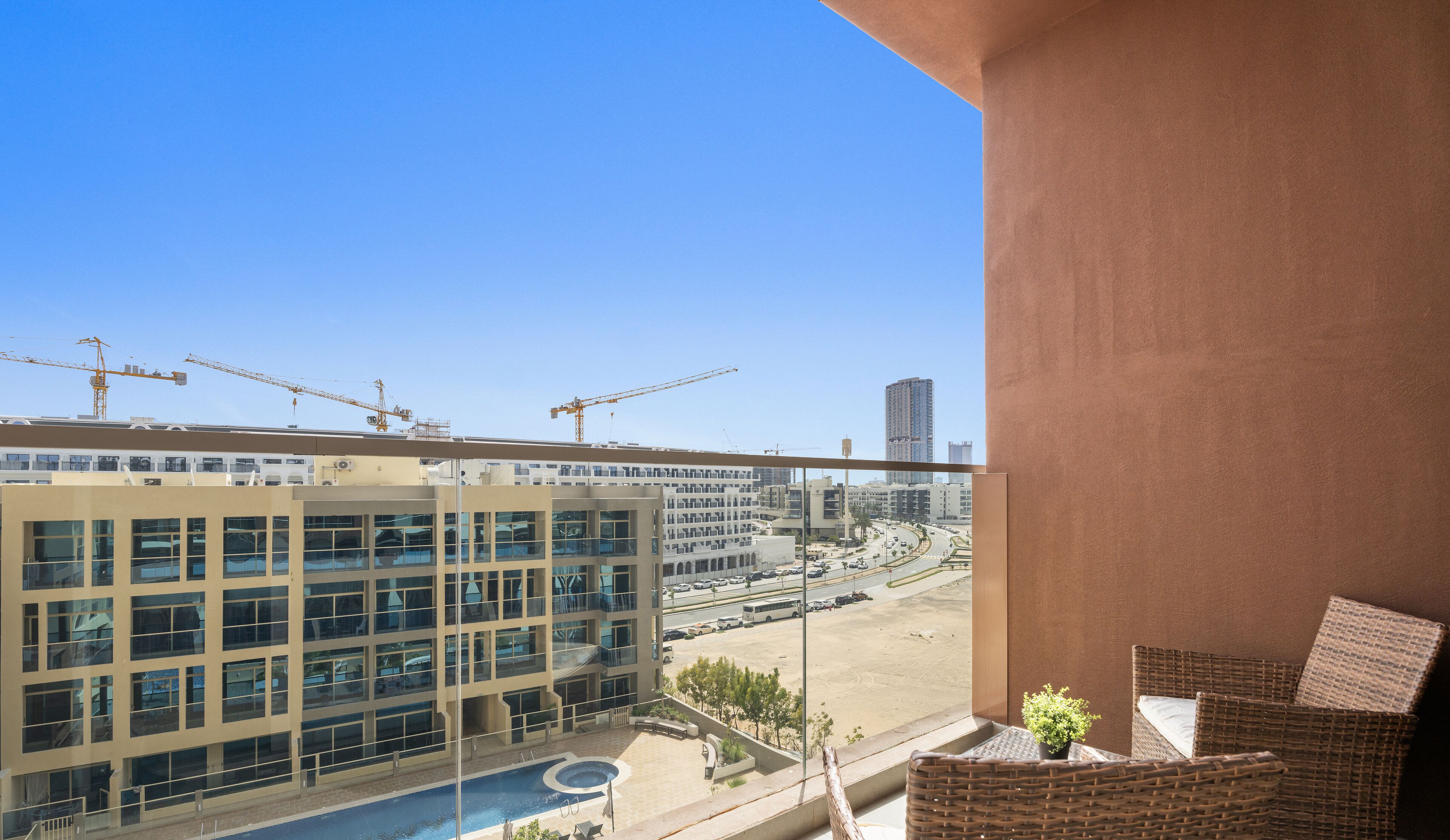 A balcony with a view of a modern building, construction cranes, and a parking lot.