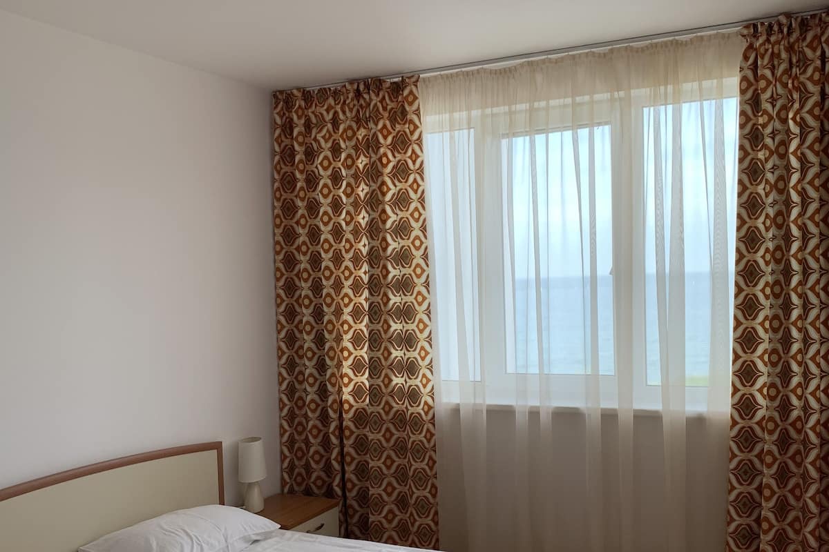 A hotel room with a bed, a nightstand, a lamp, and a window with curtains.