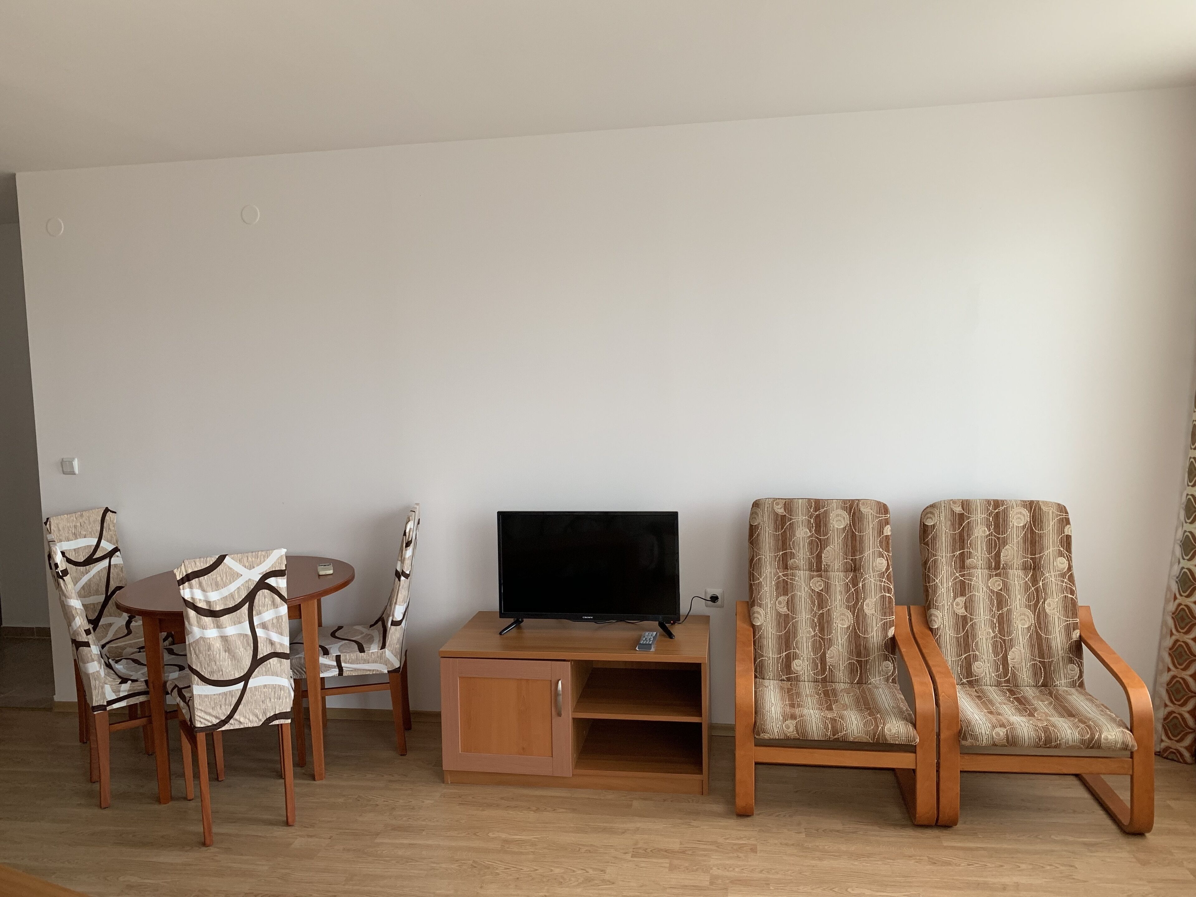 A living room with a TV, wooden cabinet, two patterned chairs, and a small table.