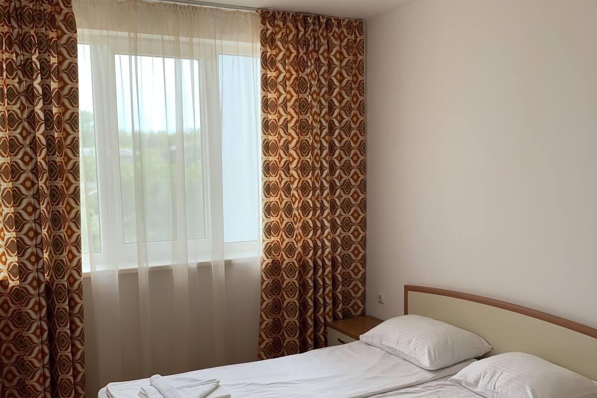 A clean, well-lit hotel room with a wooden bed, white linens, and patterned curtains.