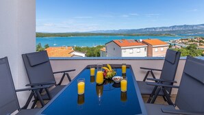 Un balcon avec une table préparée pour le petit-déjeuner, offrant une vue sur une ville côtière et les montagnes.