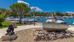 Un port de plaisance avec des bateaux amarrés, une statue et un ciel bleu azur.