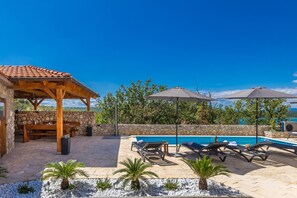 A poolside area with lounge chairs, umbrellas, and a stone wall. - Apartment DEA with heated pool and sea view (Klimno)