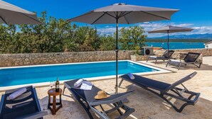 Un espace aménagé au bord de la piscine, avec des chaises longues, des parasols et une vue sur la mer.