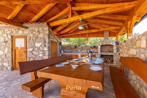 An outdoor dining area with stone walls, wooden beams, and a stone fireplace. - Apartment DEA with heated pool and sea view (Klimno)