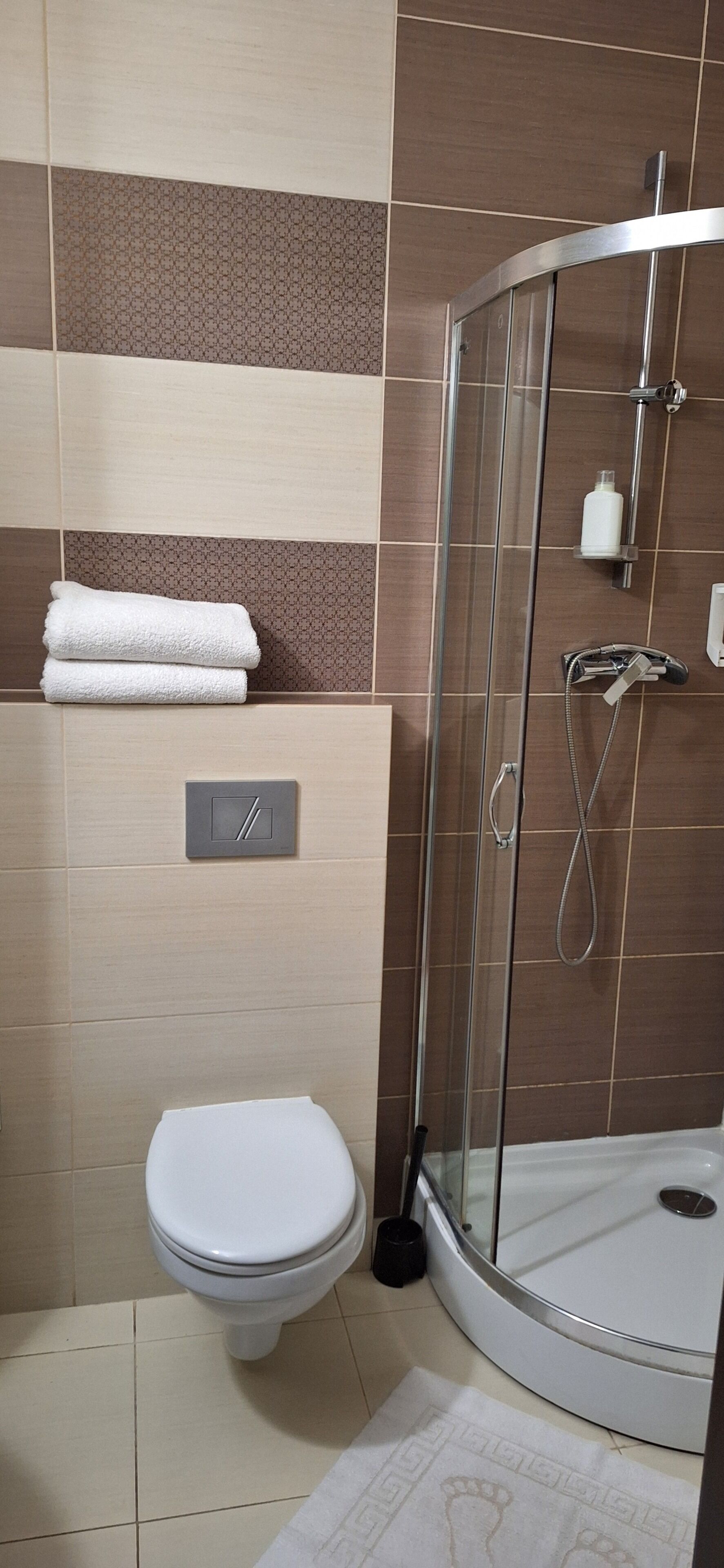A bathroom with a toilet, a glass-enclosed shower, and a towel rack with folded towels.