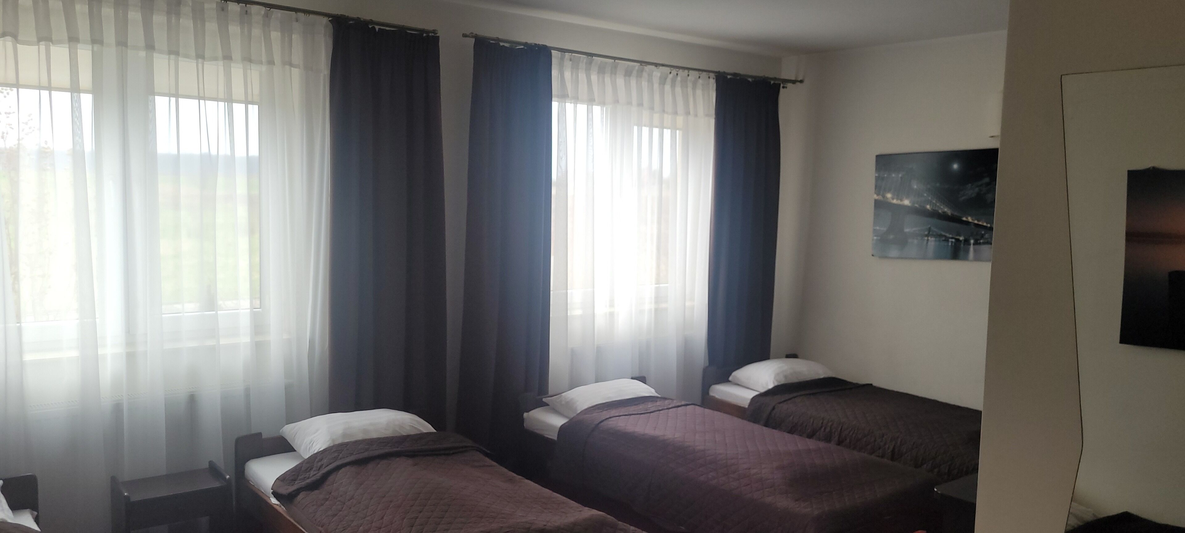 A hotel room with three single beds, a small table, and a wall-mounted TV.