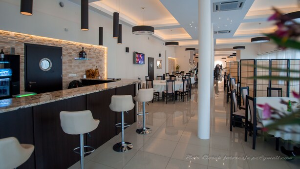 A modern bar area with a stone accent wall, a round mirror, and a television. There are bar stools and a seating area with tables and chairs. - Hotel Graal (gmina Klaj)