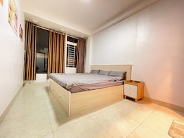 Un dormitorio con cama, mesita de noche y ventana con cortinas.