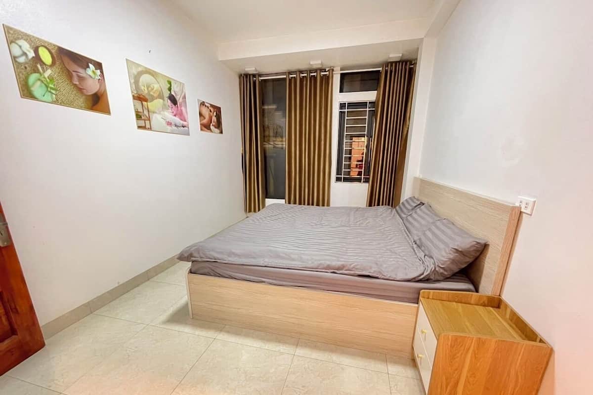A bedroom with a bed, a wooden nightstand, a window with curtains, and wall art.