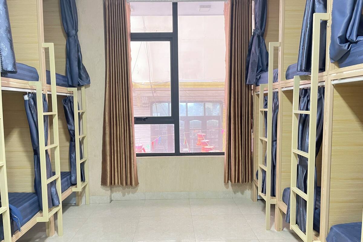 A dormitory room with bunk beds, a window with curtains, and a tiled floor.