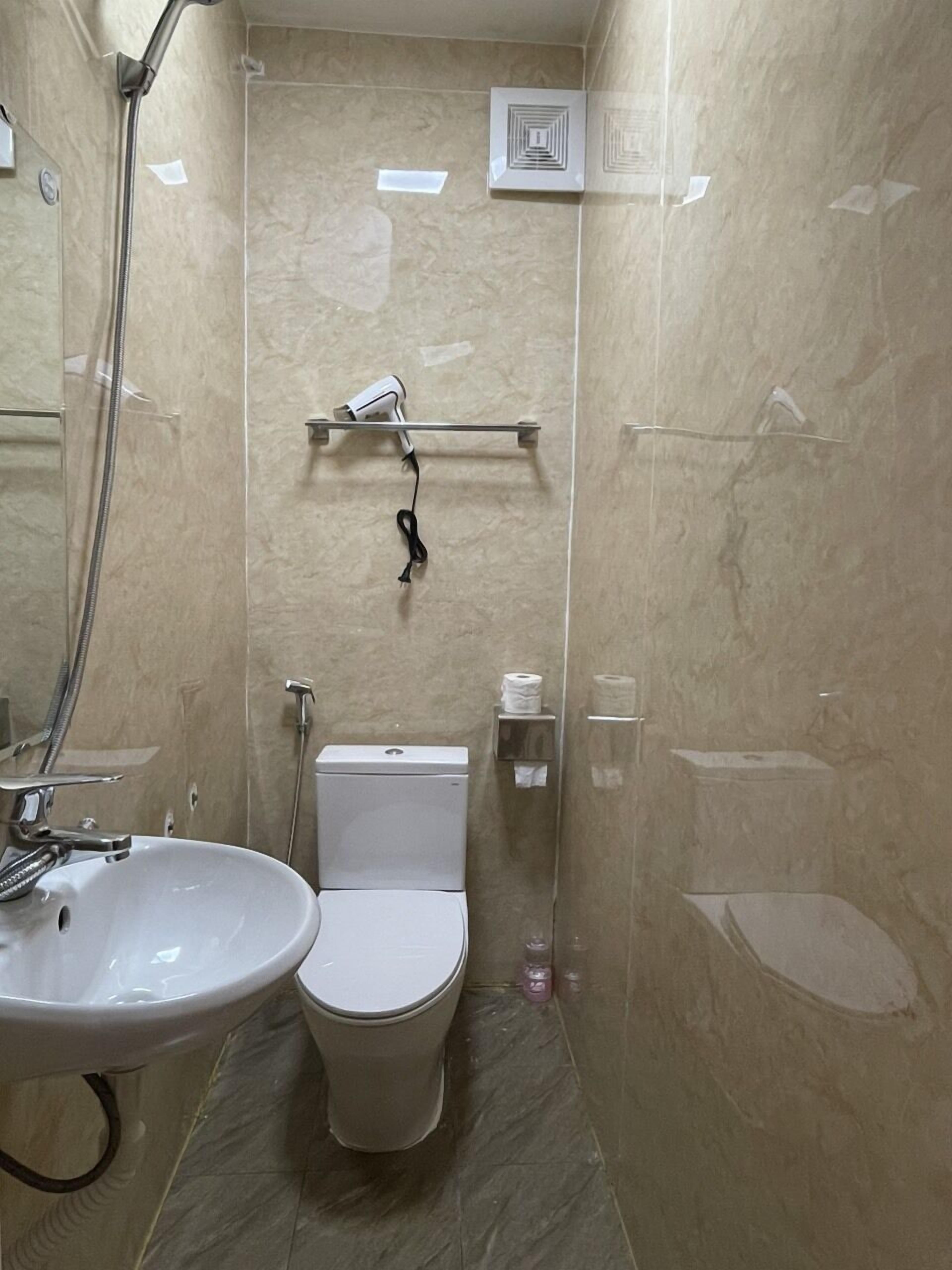 A bathroom with a white sink, toilet, and shower. There is a hairdryer on a rack above the toilet.