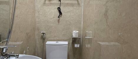 A bathroom with a white sink, toilet, and shower. There is a hairdryer on a rack above the toilet.