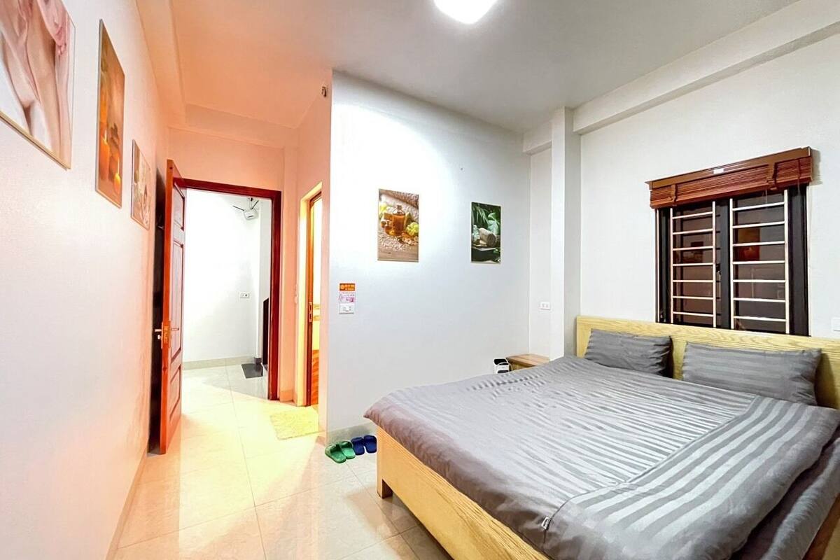 A bedroom with a bed, a nightstand, a window with blinds, and a door leading to another room.