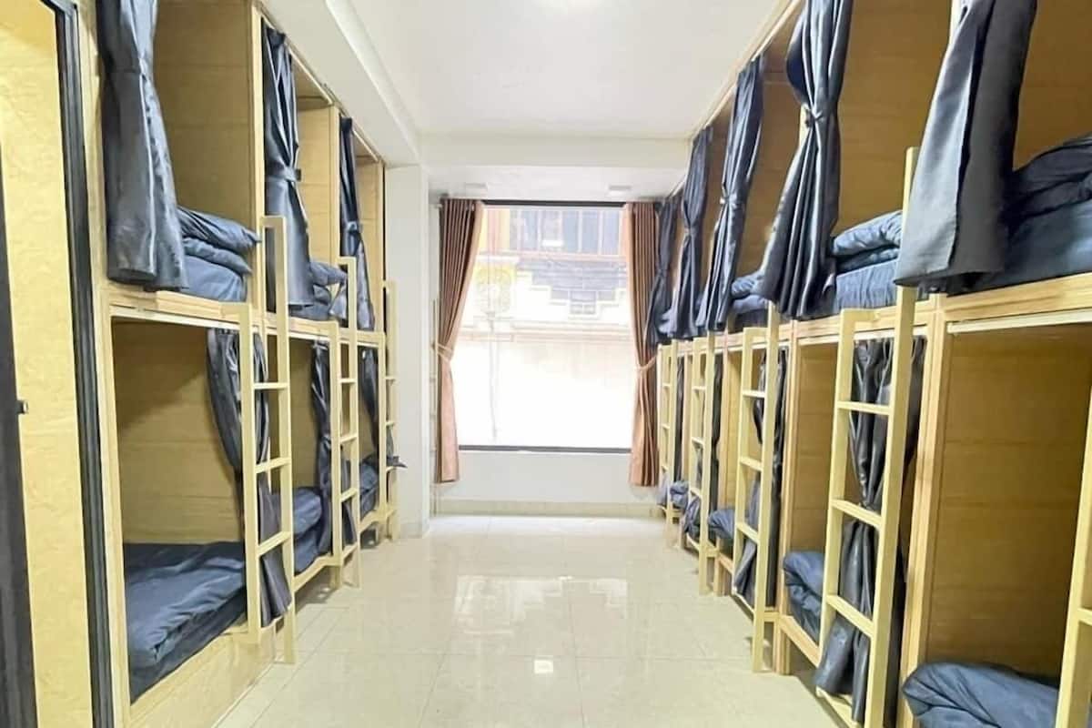 A corridor with bunk beds aligned on both sides, leading to a window with curtains.