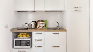 Una cocina moderna con armarios blancos, un hervidor de acero inoxidable, una caja de pasta italiana, un fregadero y un microondas.