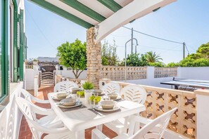 An outdoor patio with a table set for dining, surrounded by white chairs, a stone pillar, and a wooden fence.