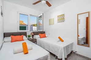 Een hotelkamer met twee bedden, een plafondventilator, een raam met uitzicht en een spiegel aan de muur.