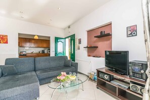 A living room with a grey sofa, a glass coffee table with flowers, a TV, and a sound system.