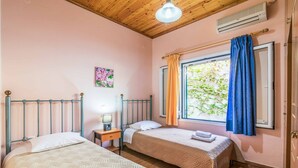 Un dormitorio con dos camas, una ventana con cortinas, una mesita de noche con lámpara y aire acondicionado instalado en la pared.