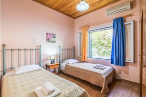 Ein Schlafzimmer mit zwei Betten, einem Fenster mit Vorhängen, einem Nachttisch mit Lampe und einer wandmontierten Klimaanlage.
