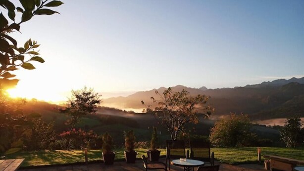 An outdoor patio with wooden tables and chairs, overlooking a valley with mountains in the distance. - Heredad de la Cueste (Llenín)