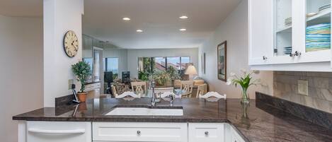 A modern kitchen with white cabinets, a granite countertop, and a large window.