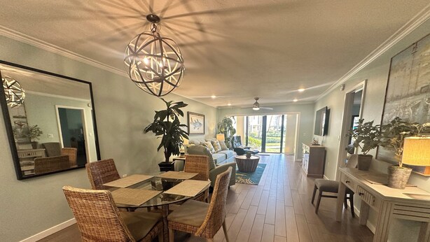 Een ruime eethoek met een glazen tafel en rieten stoelen, een grote potplant en een moderne kroonluchter.