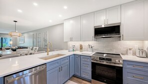 Una cocina moderna con armarios blancos, electrodomésticos de acero inoxidable y un comedor con mesa y sillas blancas.