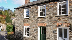A stone cottage with a green door, multiple windows, and a chimney. - Lowen Cottage (Boscastle)