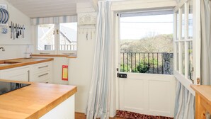 A kitchen with wooden countertops, a sink, and a window with curtains. - Lowen Cottage (Boscastle)