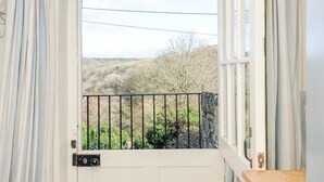 A room with a white door, a window with a view of a garden and hills. - Lowen Cottage (Boscastle)