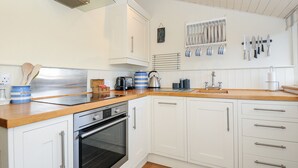 A modern kitchen with white cabinetry, a stainless steel oven, a glass range hood, and a wooden countertop. - Lowen Cottage (Boscastle)