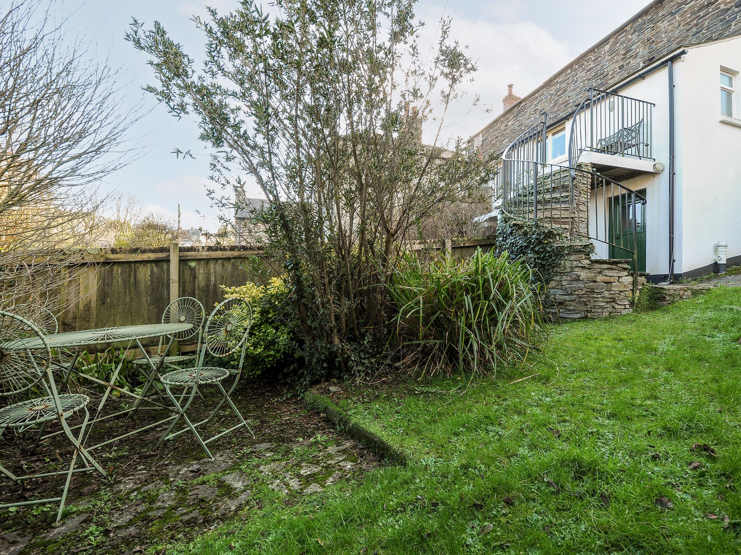 A garden with a stone wall, a wooden fence, and a metal table with chairs.