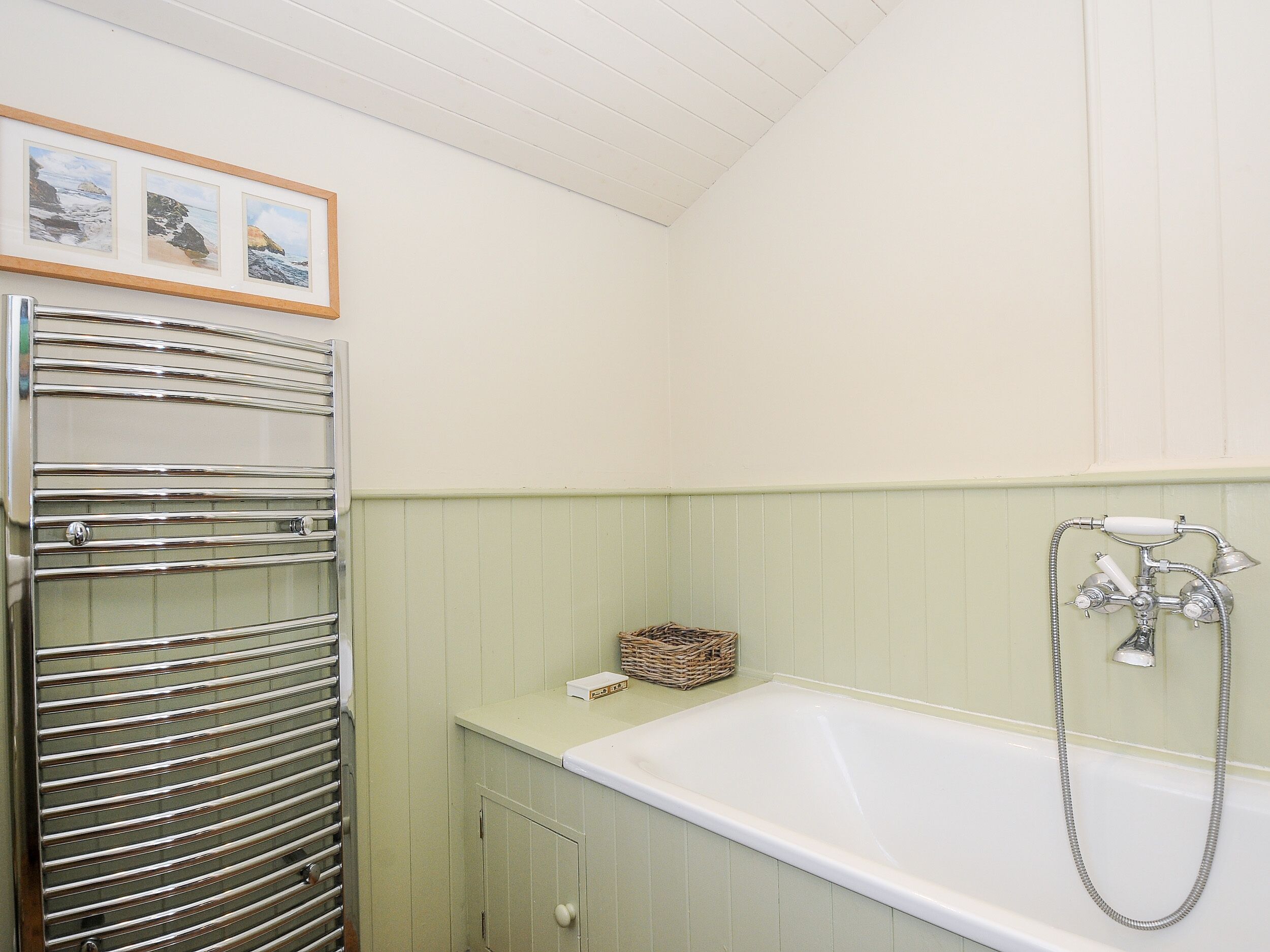 Ein Badezimmer mit einer weißen Badewanne, einem chromfarbenen Handtuchhalter und einem Korbwäscheschrank auf der Ablagefläche.