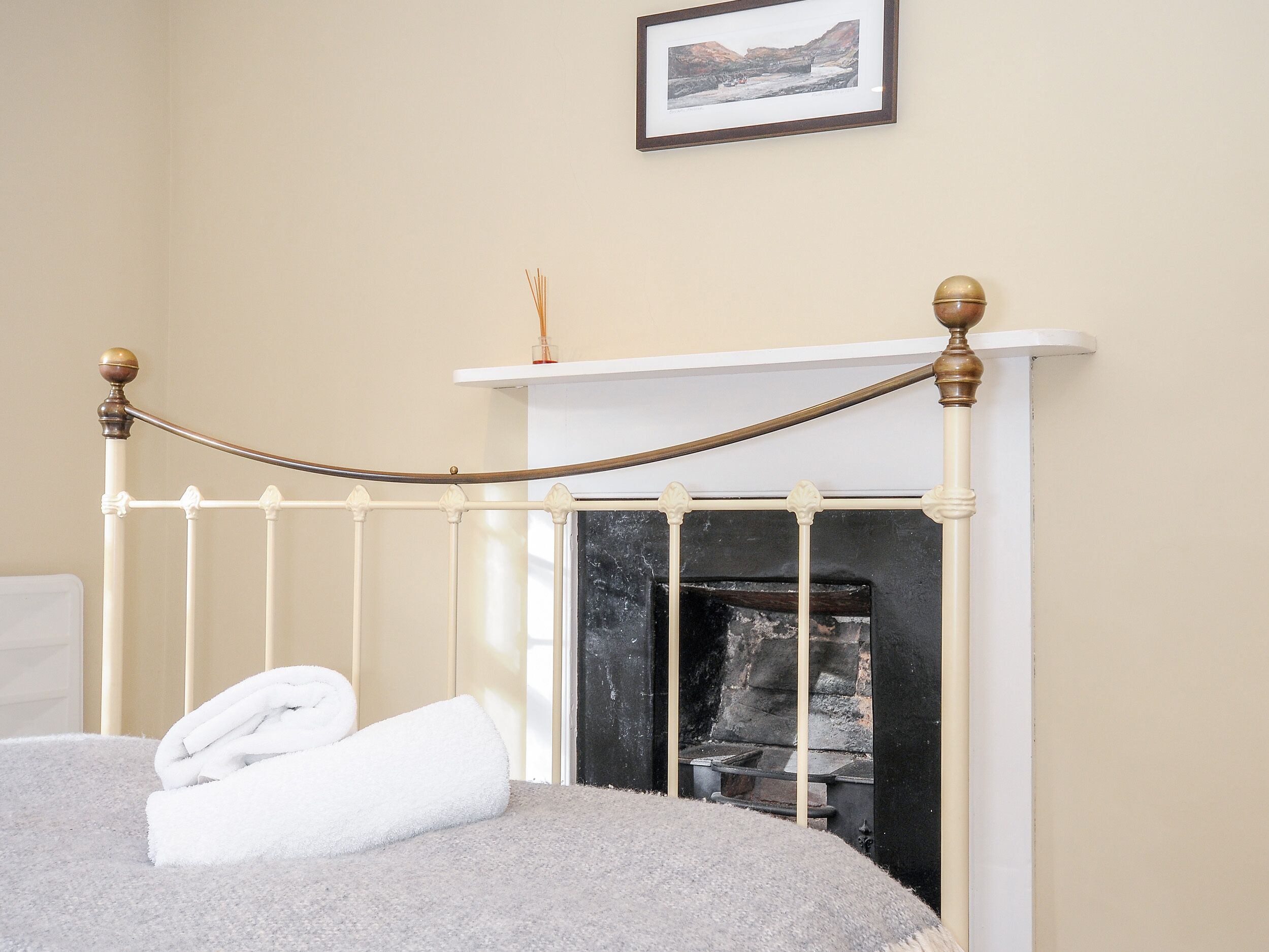 Un dormitorio con estructura de cama de metal blanco, chimenea blanca y un cuadro en la pared.