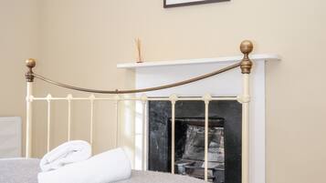 Un dormitorio con estructura de cama de metal blanco, chimenea blanca y un cuadro en la pared.