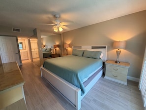 A bedroom with a bed, bedside tables, a mirror, and a ceiling fan.