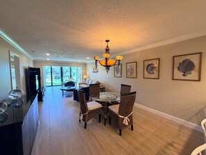 A spacious dining area with a round table and wicker chairs, a sofa, and a chandelier.
