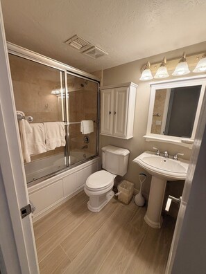 A bathroom with a glass-enclosed shower, a toilet, a sink, and a mirror.
