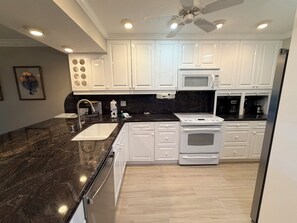 A modern kitchen with white cabinets, a black countertop, a built-in microwave, and a stainless steel dishwasher.