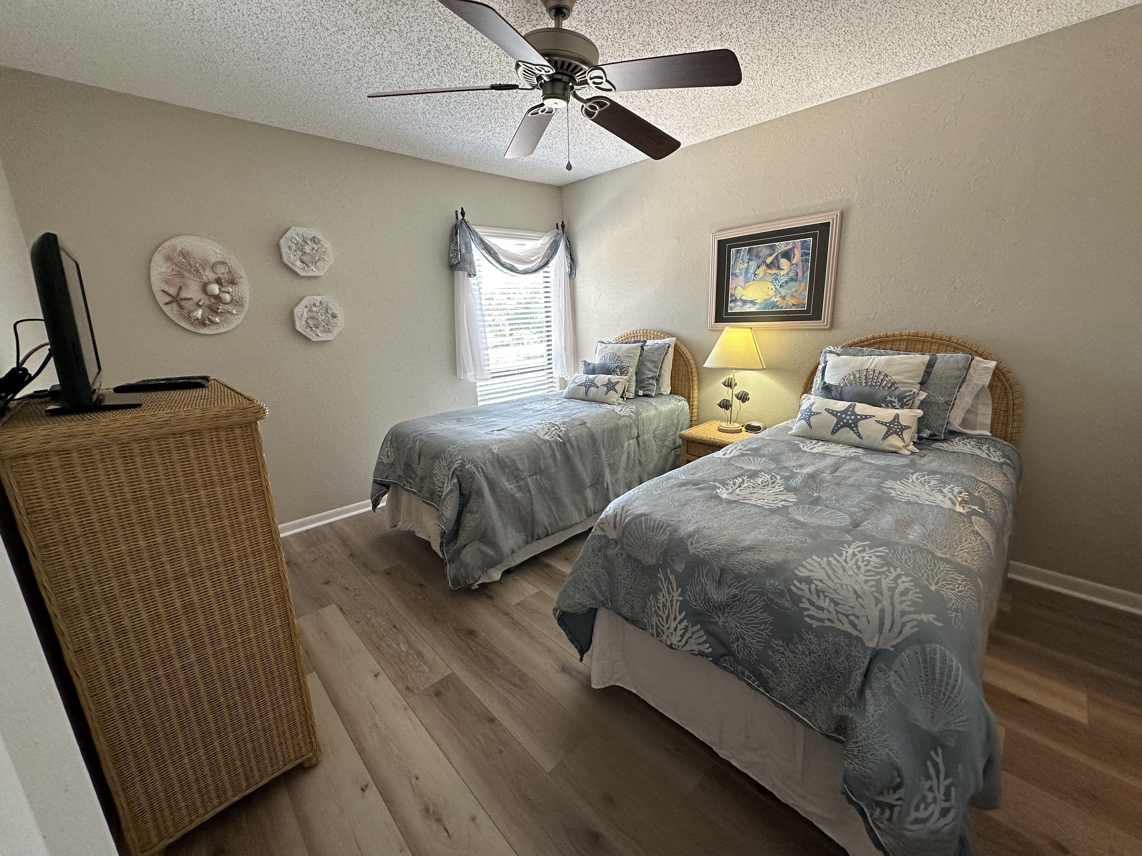 A bedroom with two beds, a ceiling fan, a television, and a window with curtains.
